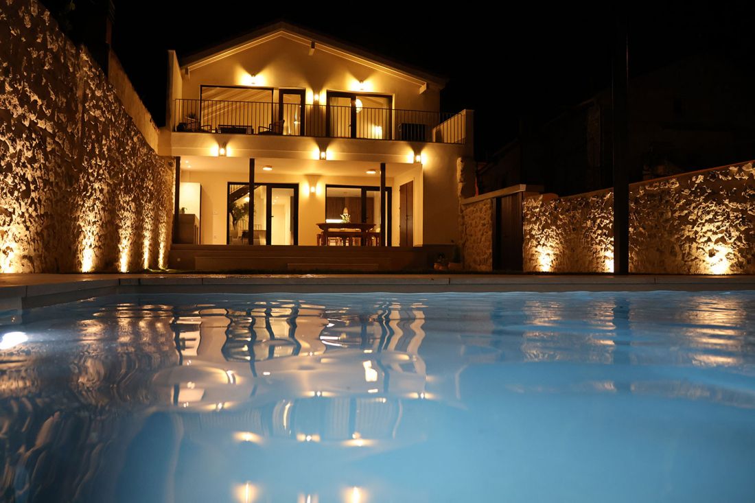 Vista nocturna del exterior de la casa y la piscina