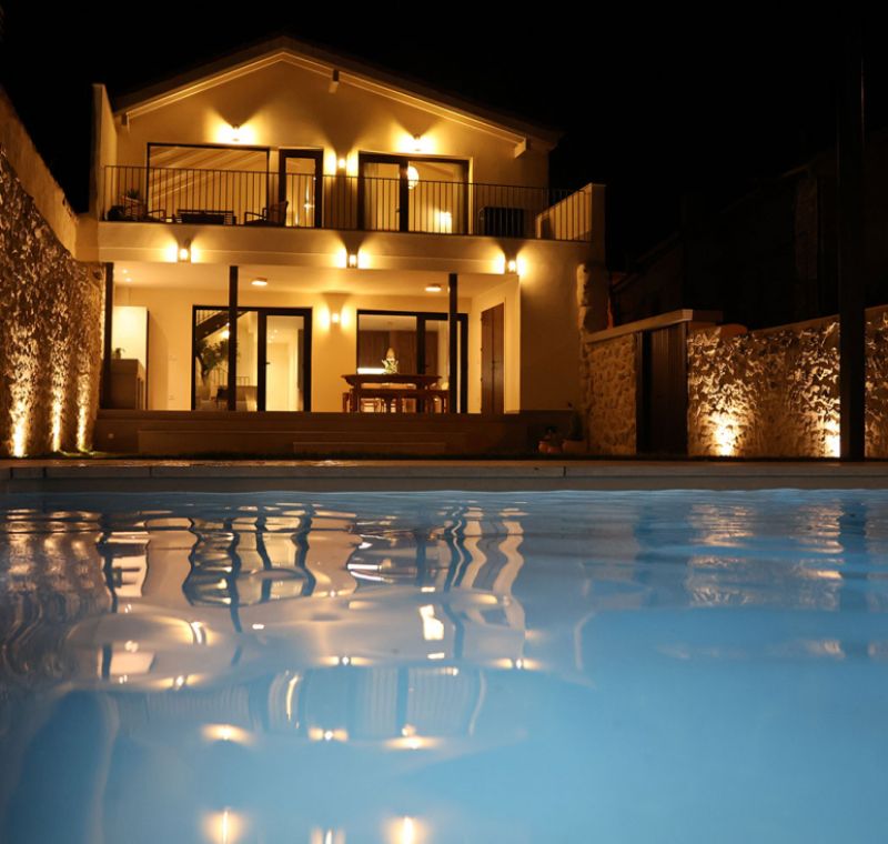 Vista nocturna del exterior de la casa y la piscina
