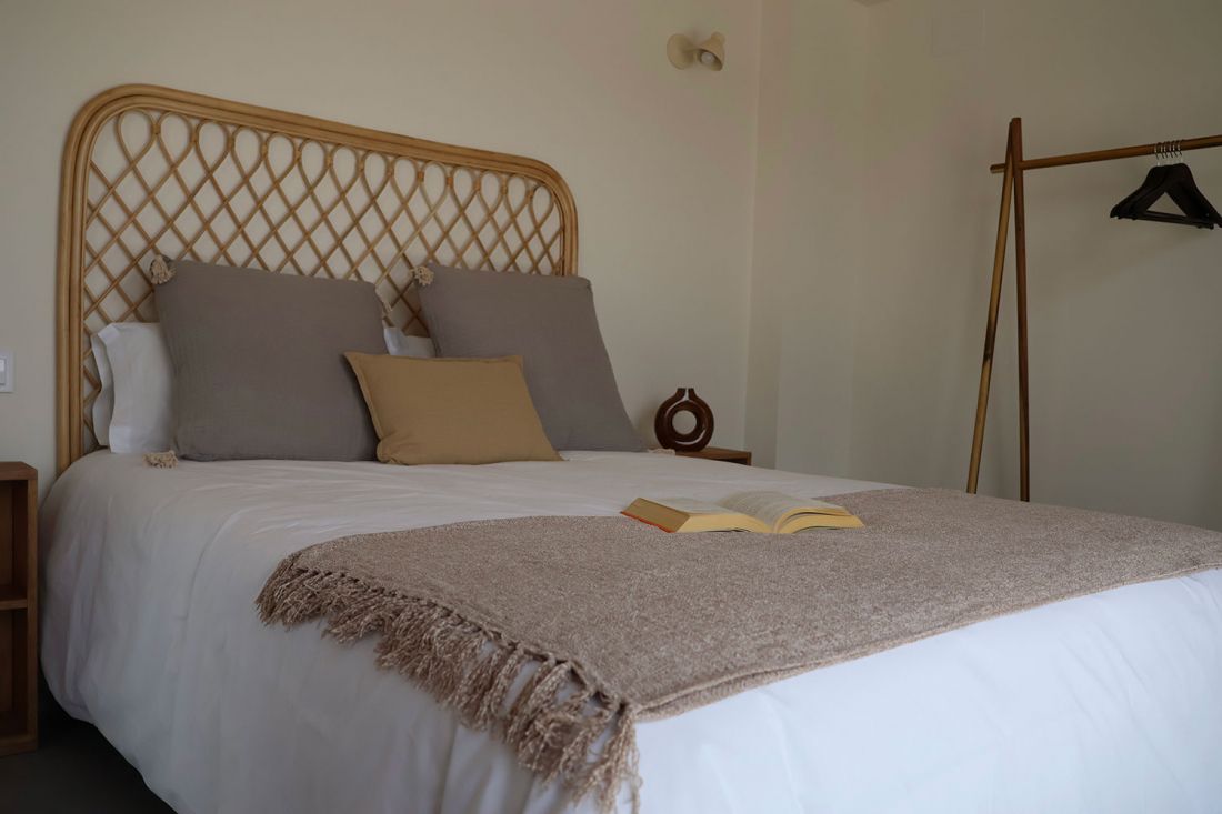 Cama con colcha blanca y cabecero de madera y mimbre con colgador de madera
