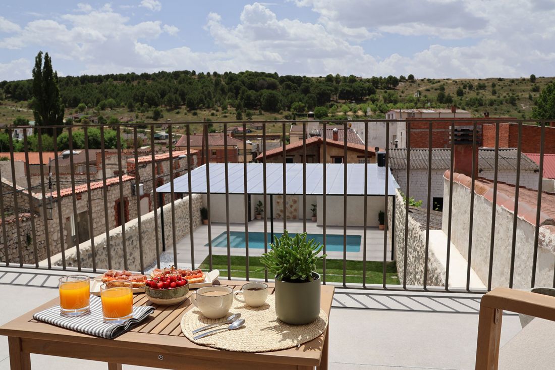Vista del jardín y piscina desde la terraza con desayuno en primer plano