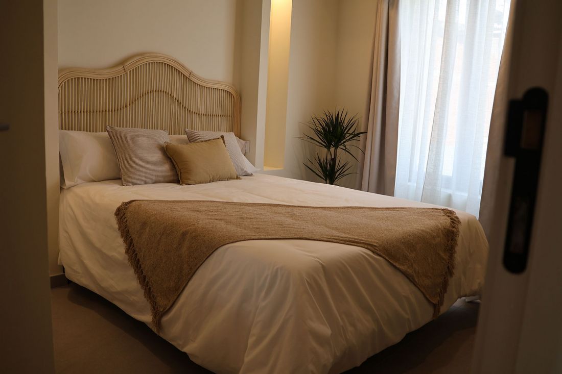 Vista de cama con cabecero de mimbre y madera en habitación minimalista en rono ocre